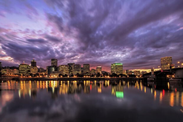 Cityscape of Portland skyline during sunset with colorful clouds and building lights reflecting on the water