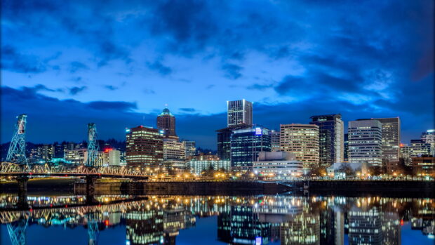 Night view of Portland skyline reflecting on calm river with city lights and bridge structures