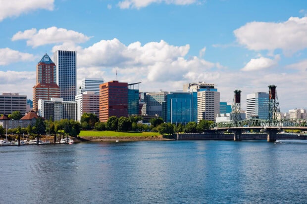 The Portland skyline with high rise buildings and a bridge over the river under a blue sky with clouds