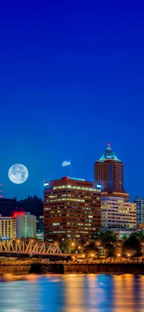 Full moon shining over Portland skyline with illuminated buildings and river reflections at night