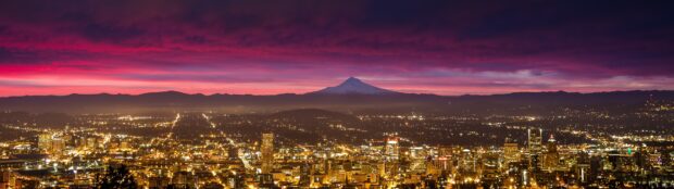 Portland skyline with illuminated buildings and Mount Hood in the background during sunset