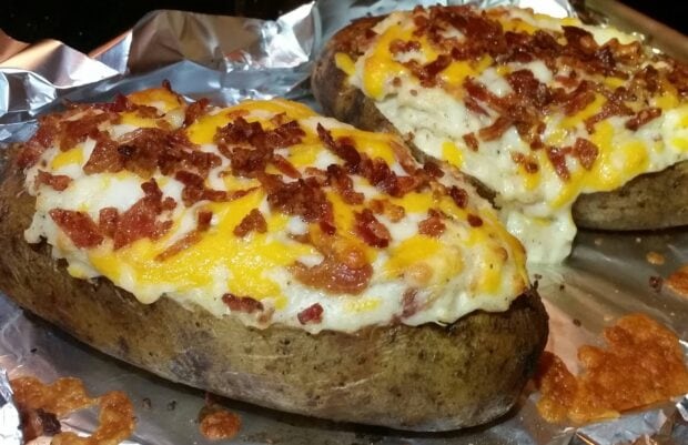 Delicious baked potato filled with creamy cheese and crispy bacon bits on foil