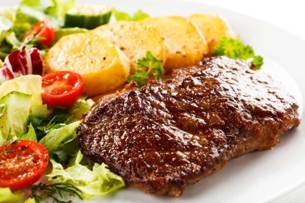 A close up of potato slices seasoned and cooked served with fresh salad and grilled meat on a white plate
