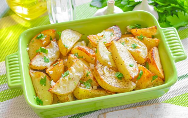 Roasted potato wedges garnished with garlic and herbs in a green baking dish