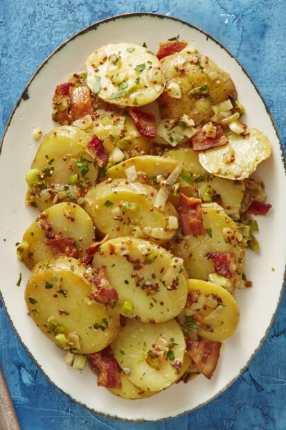 Sliced potatoes cooked with herbs and bacon on a white plate