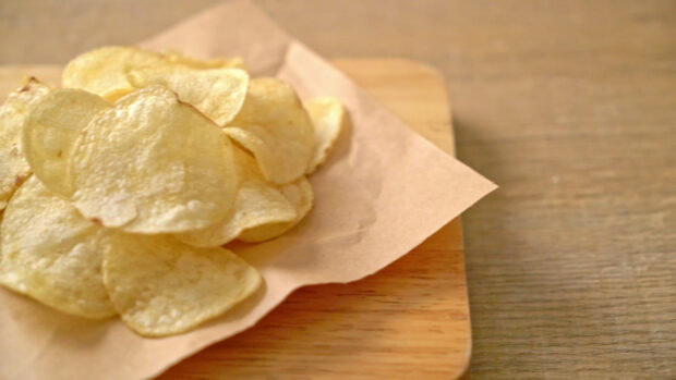 A close up of potato chips on brown paper placed on a wooden board