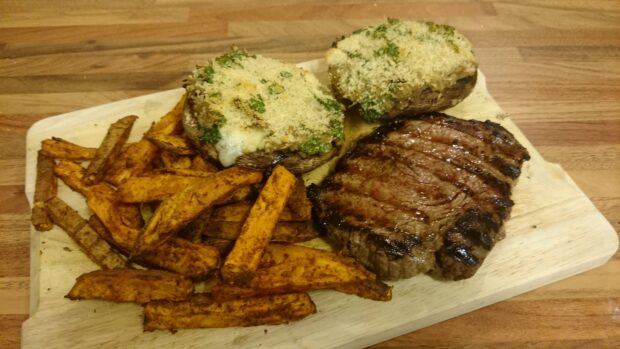 Grilled steak served with seasoned potato fries and stuffed potatoes on a wooden board