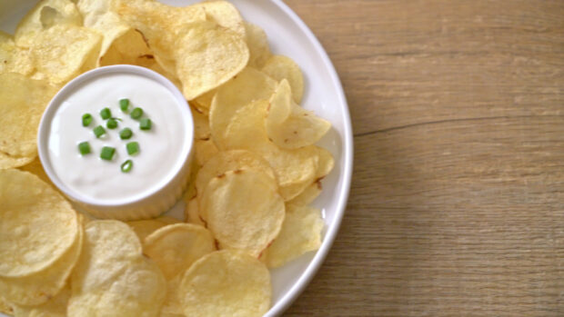 A close up of potato chips served with a bowl of sour cream and chives on a wooden table
