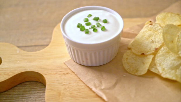 A close up of potato chips served with a bowl of sour cream topped with chopped green onions