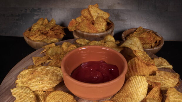 Crispy potato chips arranged around a bowl of ketchup on a wooden platter