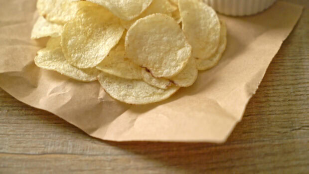 Crispy potato chips arranged on brown paper on a wooden surface