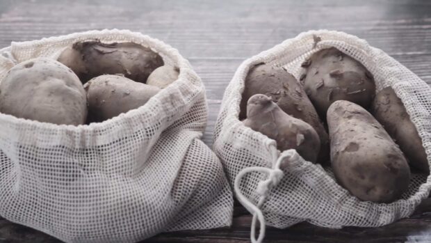 Fresh potato in mesh bags placed on wooden surface in high resolution