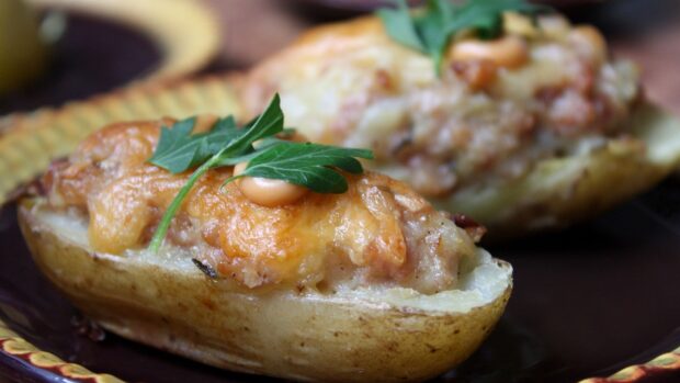Baked potato topped with melted cheese and fresh parsley leaves on a decorative plate