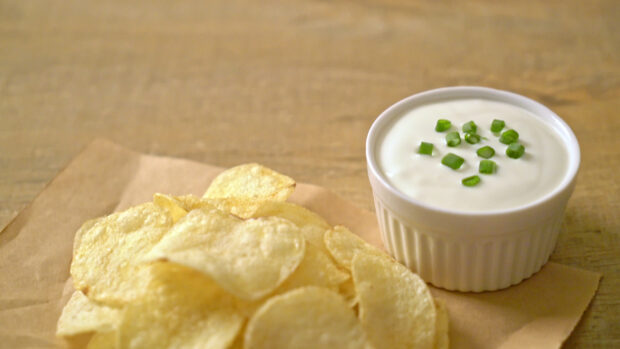 Potato chips served with a bowl of sour cream topped with chopped green onions on a wooden table