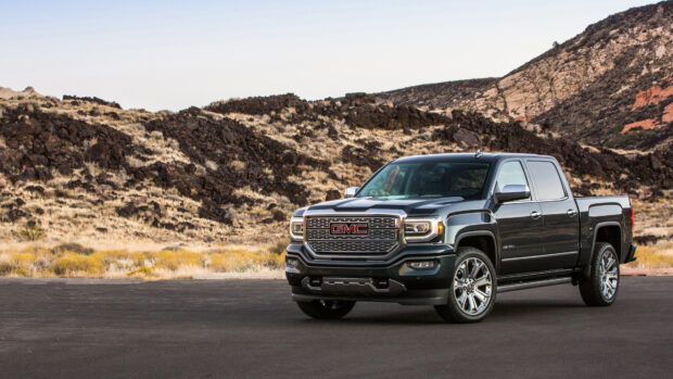 A powerful GMC truck is parked on a paved road with rocky hills in the background featuring GMC Wallpapers, 4K Desktop Wallpaper