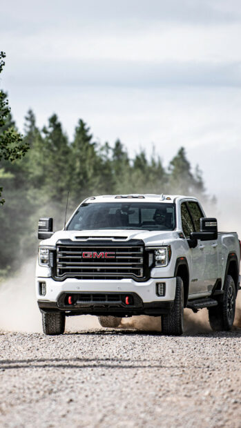 A powerful GMC truck drives through a dusty forest road with trees in the background, 2K Phone Wallpaper