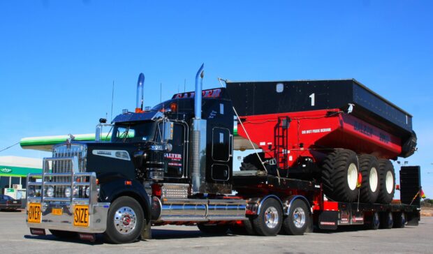 A Kenworth truck is hauling a large red and black trailer under a clear blue sky, 2K Desktop Wallpaper