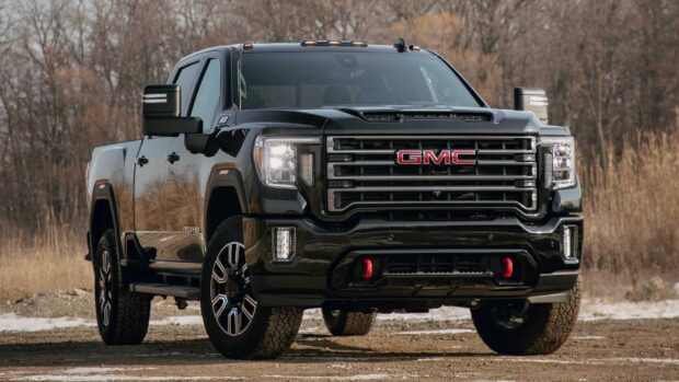 A powerful black GMC truck stands on rough terrain surrounded by dry trees and earth, HD Desktop Wallpaper