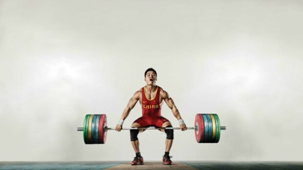 A powerlifter from China lifting a heavily loaded barbell with intense focus, HD Desktop Wallpaper