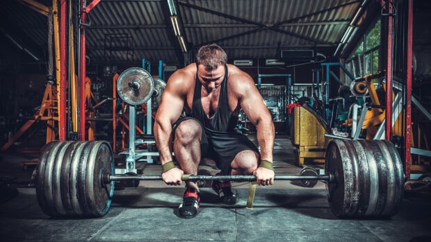 A muscular man preparing to lift a heavy barbell in a gym, 2K Desktop Wallpaper