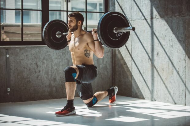 A muscular man is powerlifting with a barbell while doing lunges in a gym, 2K Desktop Wallpaper