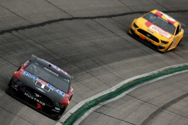 Two race cars are competing on the track with Kevin Harvick's car leading, 2K Desktop Wallpaper