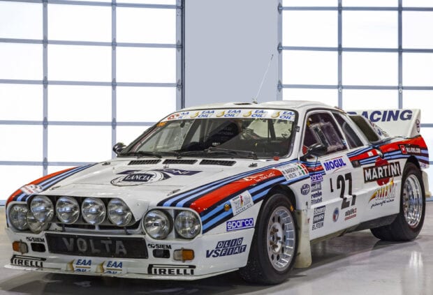 A Lancia rally car is parked inside a garage with racing decals, 2K Desktop Wallpaper