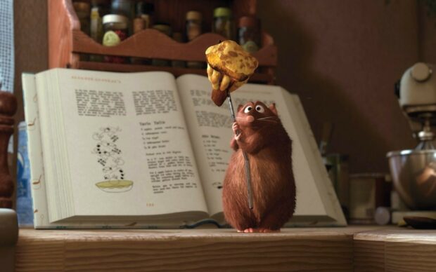 Rat holding a mushroom in front of a cookbook in a kitchen from Ratatouille