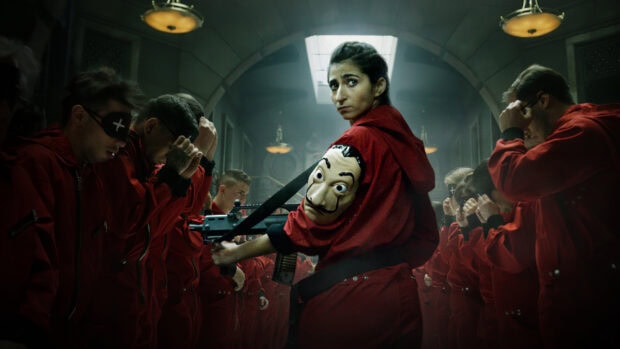 The rebel leader holds a mask and gun surrounded by captives in red suits, HD Desktop Wallpaper