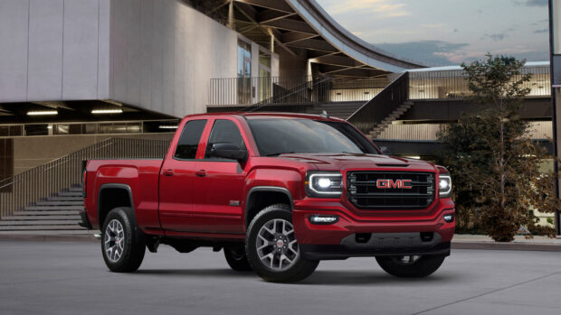 A red GMC truck is parked by the modern building at dusk with headlights on, 4K Desktop Wallpaper