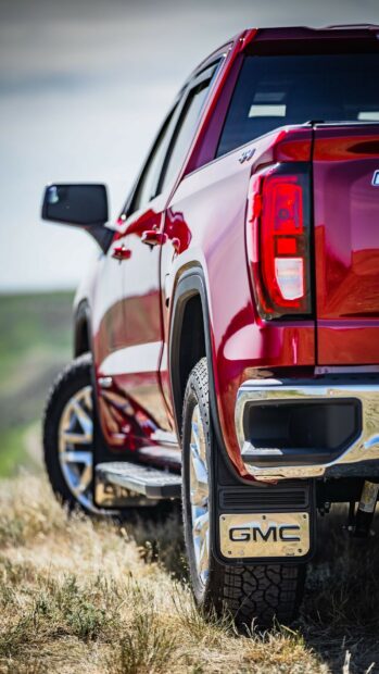 A red GMC truck is shown close up on grassy terrain under daylight, HD Phone Wallpaper