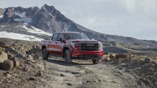 A red GMC truck is parked on a rocky mountain trail with a snowy peak in the background, 4K Desktop Wallpaper