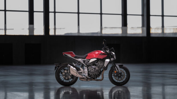 A red Honda CB1000R motorcycle stands in a spacious industrial warehouse with large windows, 4K Desktop Wallpaper