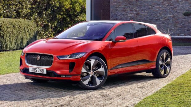 A red Jaguar I Pace is shown in a driveway with greenery and a modern wall in the background, HD Desktop Wallpaper
