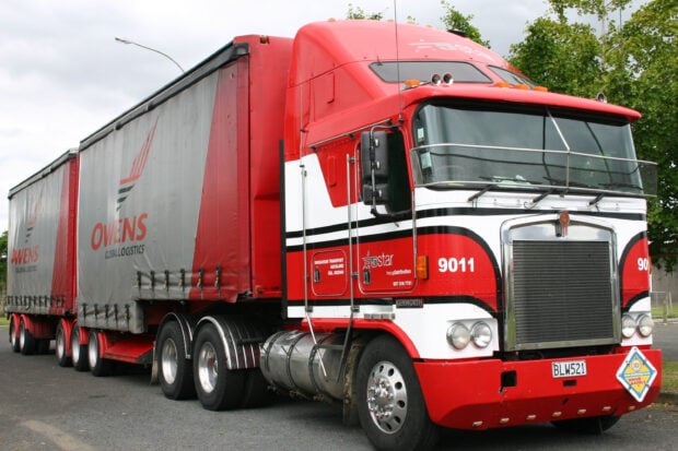A red Kenworth truck is parked with a large Owens logistics trailer on a cloudy day, 2K Desktop Wallpaper