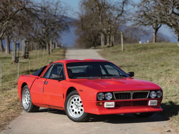 A red Lancia sports car is parked on a countryside road with trees and hills in the background, HD Desktop Wallpaper