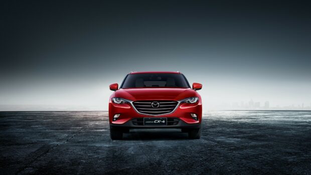 A red Mazda CX 4 car is parked on a dark textured ground with a misty city skyline in the background, 4K Desktop Wallpaper