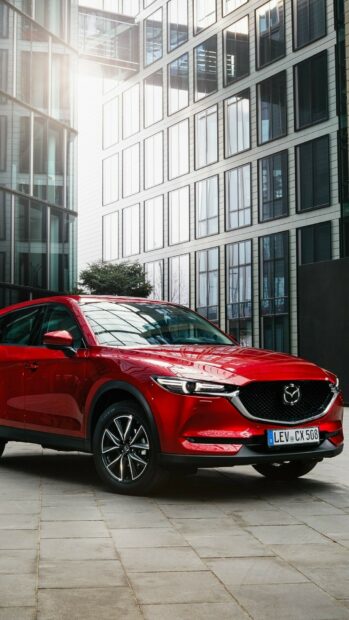 A red Mazda is parked in front of modern glass office buildings showcasing its sleek design, HD Mobile Wallpaper