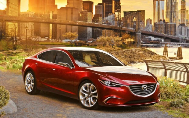 A red Mazda sedan is parked by the riverbank with a city skyline in the background in this Mazda Wallpapers, HD Desktop Wallpaper