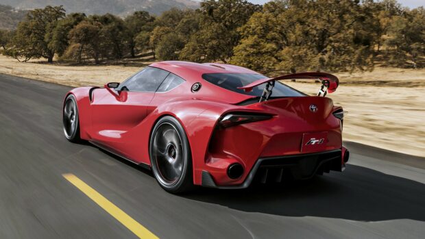 Red Toyota Supra sports car racing on open road with trees in background.