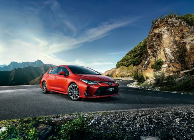 Red Toyota sedan on mountain road.