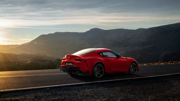 Red sports car on mountain road at sunset.