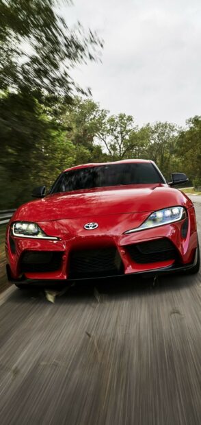 Red sports car driving on road with trees in the background.