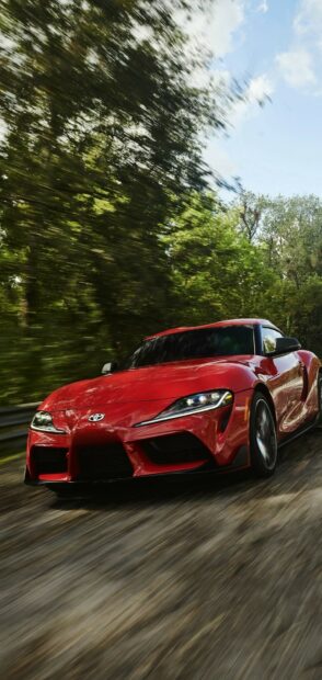 Red sports car in motion on a scenic forest road during daytime.