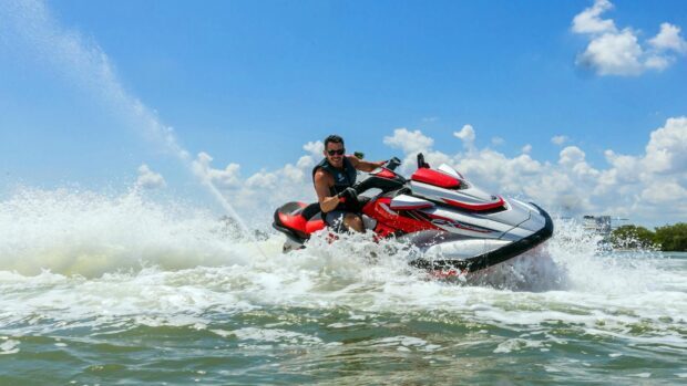 A man rides a red and silver jet ski creating water splashes under a clear blue sky, HD Desktop Wallpaper