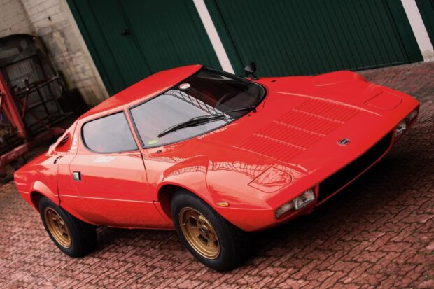 A red Lancia car is parked on a cobblestone surface beside green doors, HD Desktop Wallpaper