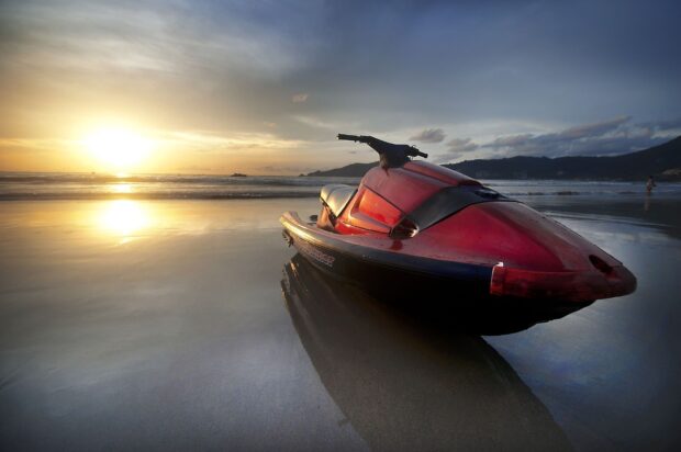 A red jet ski is parked on wet sand reflecting the sunset near the ocean shore, HD Desktop Wallpaper