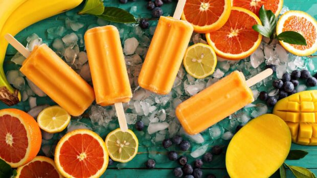Mango popsicles surrounded by fresh oranges and blueberries on ice, HD Desktop Wallpaper