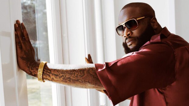 Rick Ross wears sunglasses and a maroon shirt while leaning on a window, 2K Desktop Wallpaper
