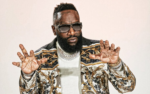 Rick Ross in a luxury patterned jacket with sunglasses and jewelry posing with hands raised, 2K Desktop Wallpaper